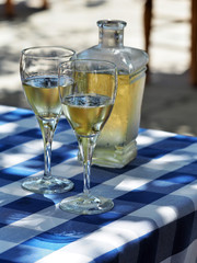 Two glasses and bottle of white wine on table with checked blue and white  tablecloth.