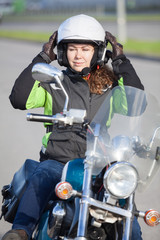 Beautiful motorcyclist woman spruces oneself up while sitting on bike and looking at back mirror