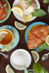 Cup of herbal tea with lemon and mint leaves, ginger root and croissant on the wooden background