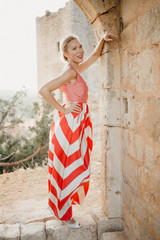 A pretty beautiful stylish blonde woman in the red dress posing in the ancient stone arch of the castle. Spain