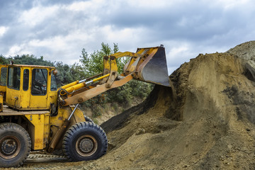 Wheel loader Excavator with backhoe unloading sand at eathmoving works in construction site quarry