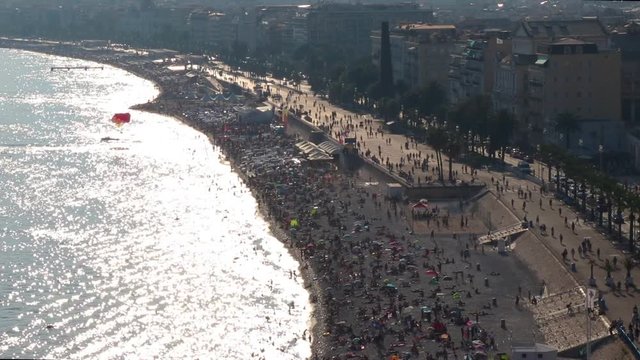 Crowded beach, Old Town, and Promenade des Anglais in Nice, southern France. Parasail lands on water. Scene of the 2016 terrorist attack. Sun reflects in the water. Establishing shot.