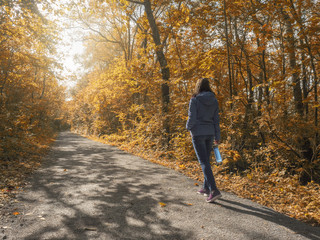 Fototapeta premium Woman walking in autumn park with a bottle of water in her hand, concept fall season, sport, health, fresh air activities, outdoor. 