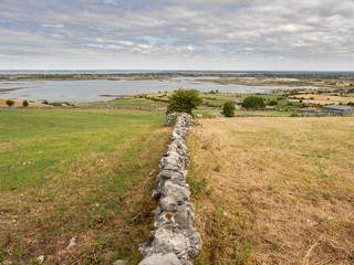 Fototapeta na wymiar Dry stone fence splits field, Galway bay in the background, Burren national park, Ireland.