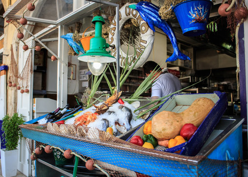 Fototapeta Fresh healthy colorful vegetables fish anf wine on wooden table on the street, Greece.