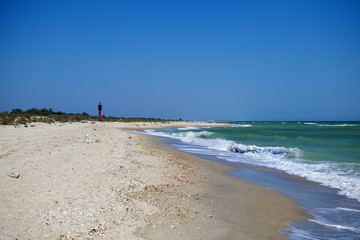 Fototapeta na wymiar Sea waves lick the sandy coast. To the left is a lighthouse in the distance (Ukraine, Black Sea, Rasseika)