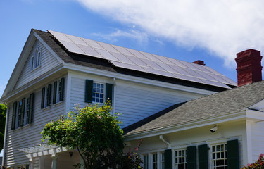 Solar panels on the roof of a traditional Colonial style house beneath a blue summer sky