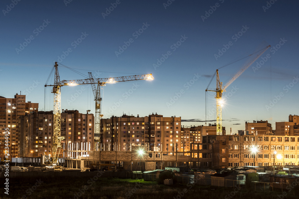 Wall mural building site with three tower cranes against the background of multi-storey houses and a blue sky, 