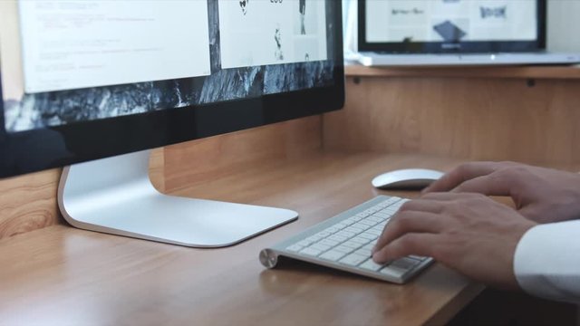 Programmer or freelancer typing with wireless keyboard at wooden desk with laptop and computer