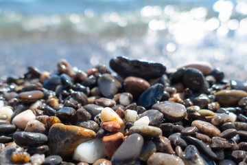 Beautiful wet colored sea pebbles on beach / Wet pebbles on sea beach on background of splashing sea in sunny summer day