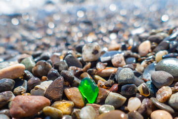 Green polished glass pebble on sea beach / Small green polished glass stone among pebbles on sea...
