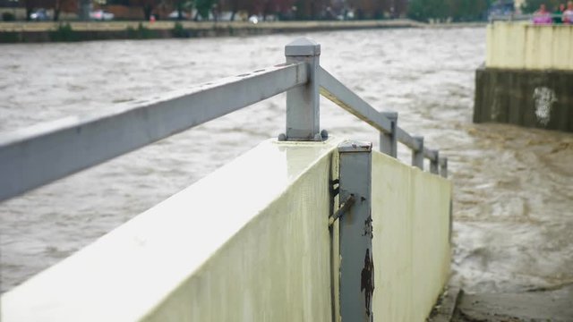 Gray opaque river waters quickly flow in the riverbed by a fenced dam in the city center, Rainy weather, flood on the canal, 4k, slow-motion