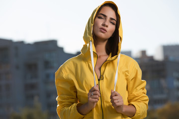 Confident woman outdoor portrait at city background in yellow windbreaker under hood