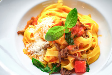 pasta tagliatelle with pieces of beef, tomatoes and Basil on white plate