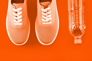 Orange sneakers with a bottle of water on a orange background.