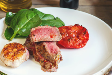 Steak with blood medium rare with a side dish of tomatoes and vegetables with spinach sauteed in a homemade pan on a wooden table.
