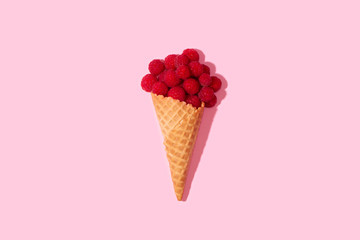 Raspberries in an ice cream cone on a table on a pink background.