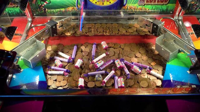 High angle shot of coin pusher game machine slowly moving to push coins of the edge