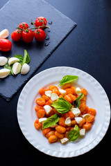 Potato gnocchi alla Sorrentina in tomato sauce with green fresh basil and mozzarella balls served on a plate