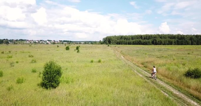 Pushkin district, Moscow region, Russia - July 7, 2018. Young adult woman riding a bicycle on a rural road. Aerial view