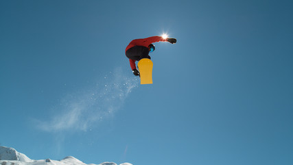 SLOW MOTION: Pro snowboarder jumping and flying over sun in winter ski resort
