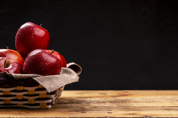 Bunch of wet red apples lying in braided bowl on black background