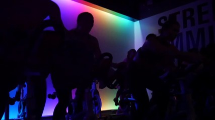 Participants in spin class ride stationary bikes in the dark with pulsating lights.