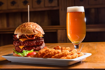 Hamburger double burger cheese bacon tomato lettuce beer onion rings wooden table
