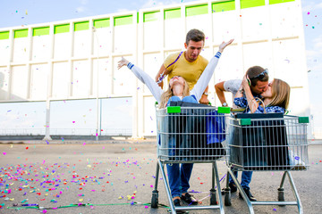 Two Boyfriends are taking their girlfriends outdoors on shopping carts in a hurry for a sale in the...