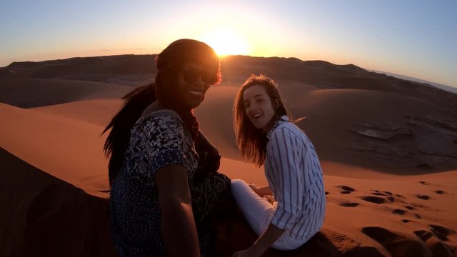Women pose in front of desert sunset, POV