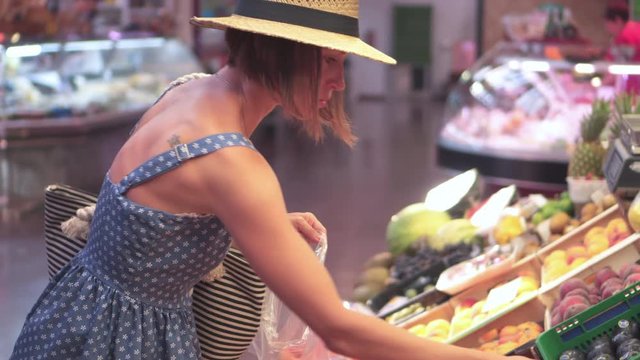 Attractive young woman choosing peaches at marketplace