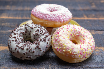 Colorful sweet glazed donuts from bakery on black wooden background close up