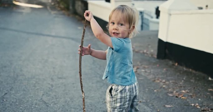 Little toddler running with stick in the street