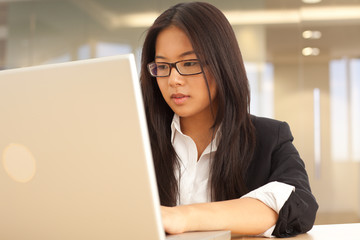 Attractive young Asian businesswoman typing on laptop computer indoors office