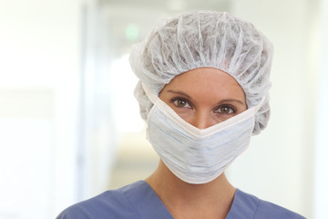 Fototapeta na wymiar Close up portrait of serious young woman doctor in scrubs with mask and cap