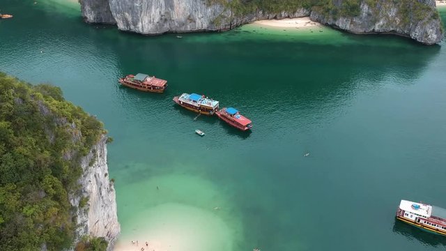 Drone footage of ships in Halong Bay, Vietnam. Green water and a sip on a boat trip in Ha Long Bay, Vietnam. People are swimming in the water.