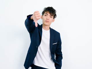 Portrait of handsome Chinese young man in dark blue leisure suit posing against white wall...