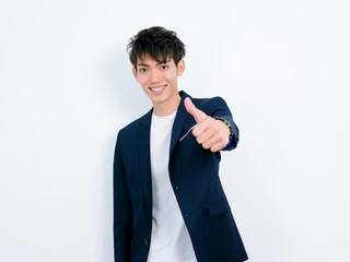 Portrait of handsome Chinese young man in dark blue leisure suit posing against white wall background. Make thumb up gesture and looks so happy.