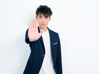Portrait of handsome Chinese young man in dark blue leisure suit posing against white wall...