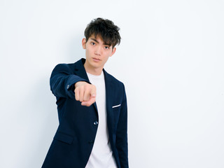 Portrait of handsome Chinese young man in dark blue leisure suit posing against white wall...
