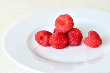 Ripe red raspberries in a pile on a white plate