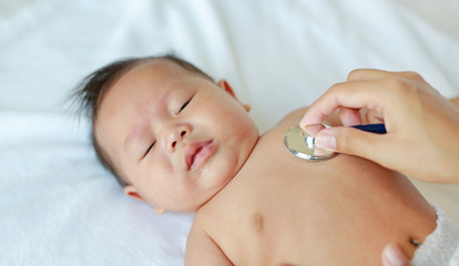 Doctor using a stethoscope to listen to baby's chest checking heart beat.