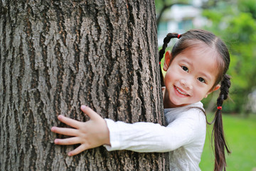 Close up of a smiling child girl embracing tree at the garden.
