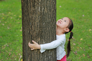 Adorable little child girl hugging a tree with looking up at the park.