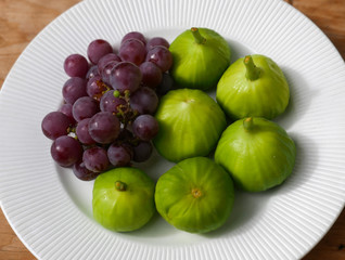 Green figs and purple grapes in a white bowl centered on wood