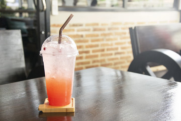 Iced Strawberry soda with straw in plastic cup on table.