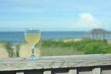A glass of white wine on railing overlooking the beach