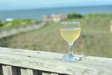 A glass of white wine on railing overlooking the beach