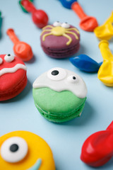 Funny children's treats for Halloween: variations of macaroon, decorated in the form of different monsters, ghosts. Cooking process. On a blue background, copy space for text, top view