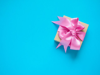 one gift box with pink satin ribbon on a blue background, copy space for text